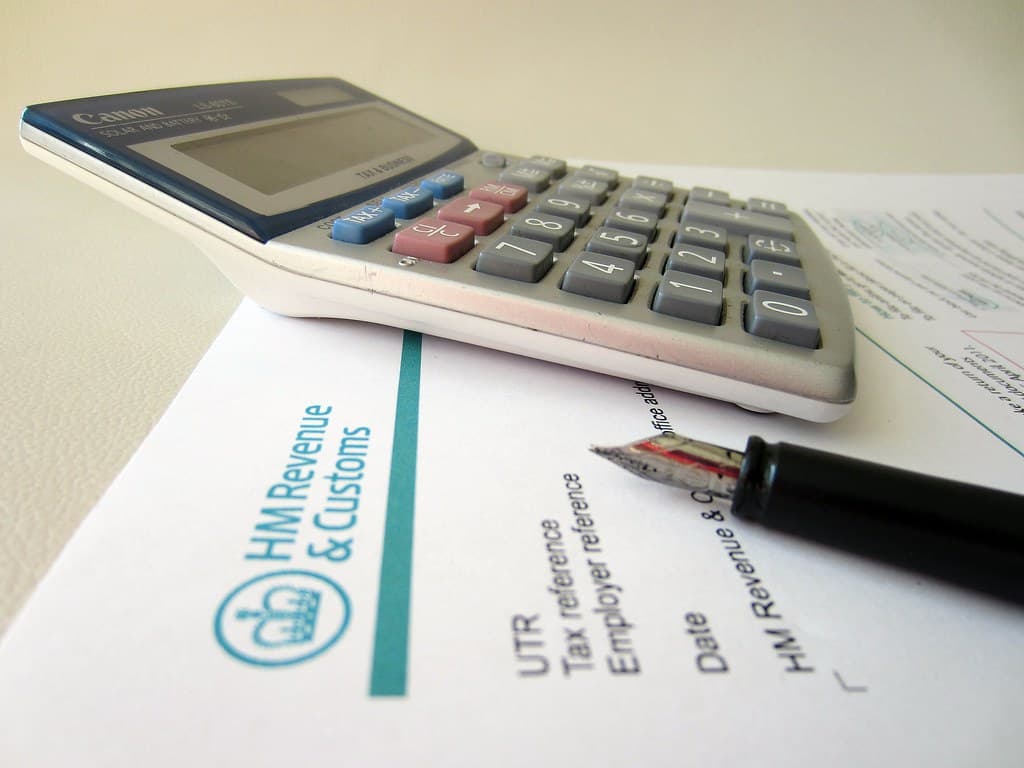 Un calculator așezat peste documente fiscale ale administrației britanice HM Revenue & Customs, cu un pix alături. (Foto de arhivă: 401(K) 2013 / BY-SA 2.0, Openverse)