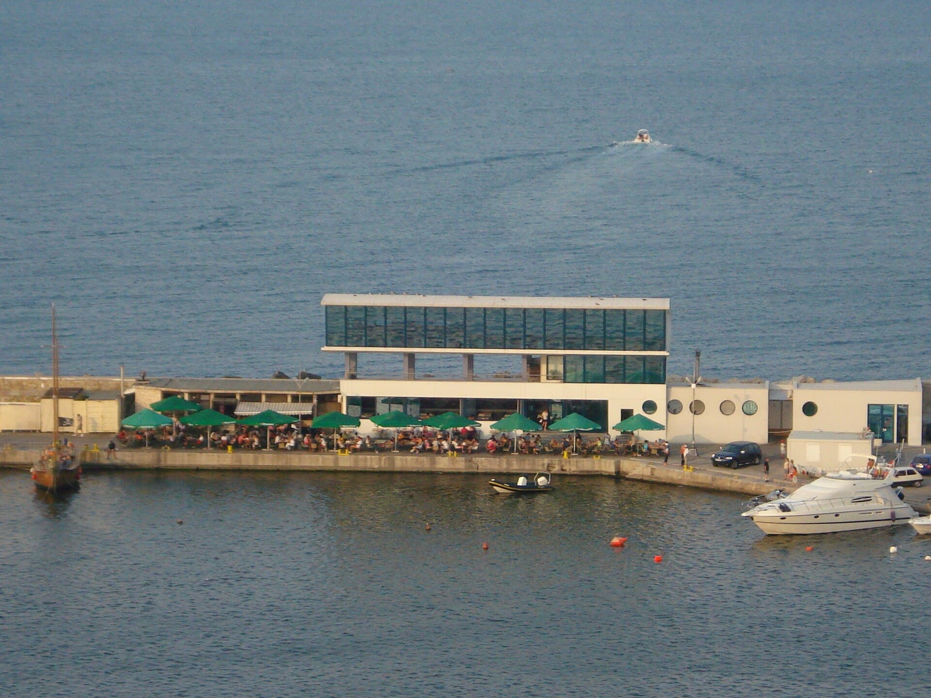 Se vede un terminal portuar pe malul mării, cu ambarcațiuni în apropiere. (Foto: Razvan85 / CC BY-SA 3.0, Wikimedia Commons)