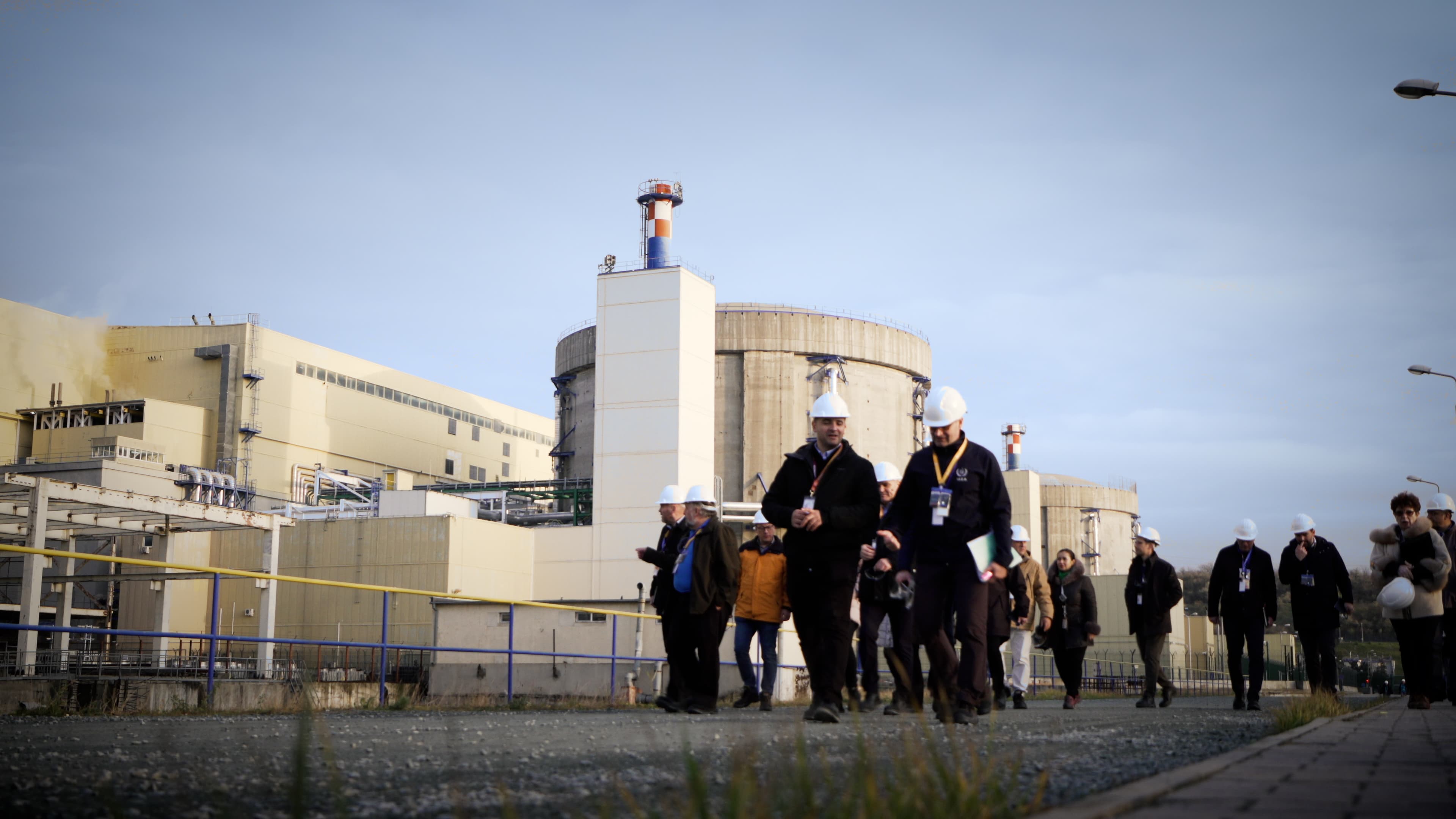 Se vede o centrală nucleară, cu mai multe persoane în prim-plan, în exteriorul complexului. (Foto: IAEA Imagebank / BY 2.0, Openverse)