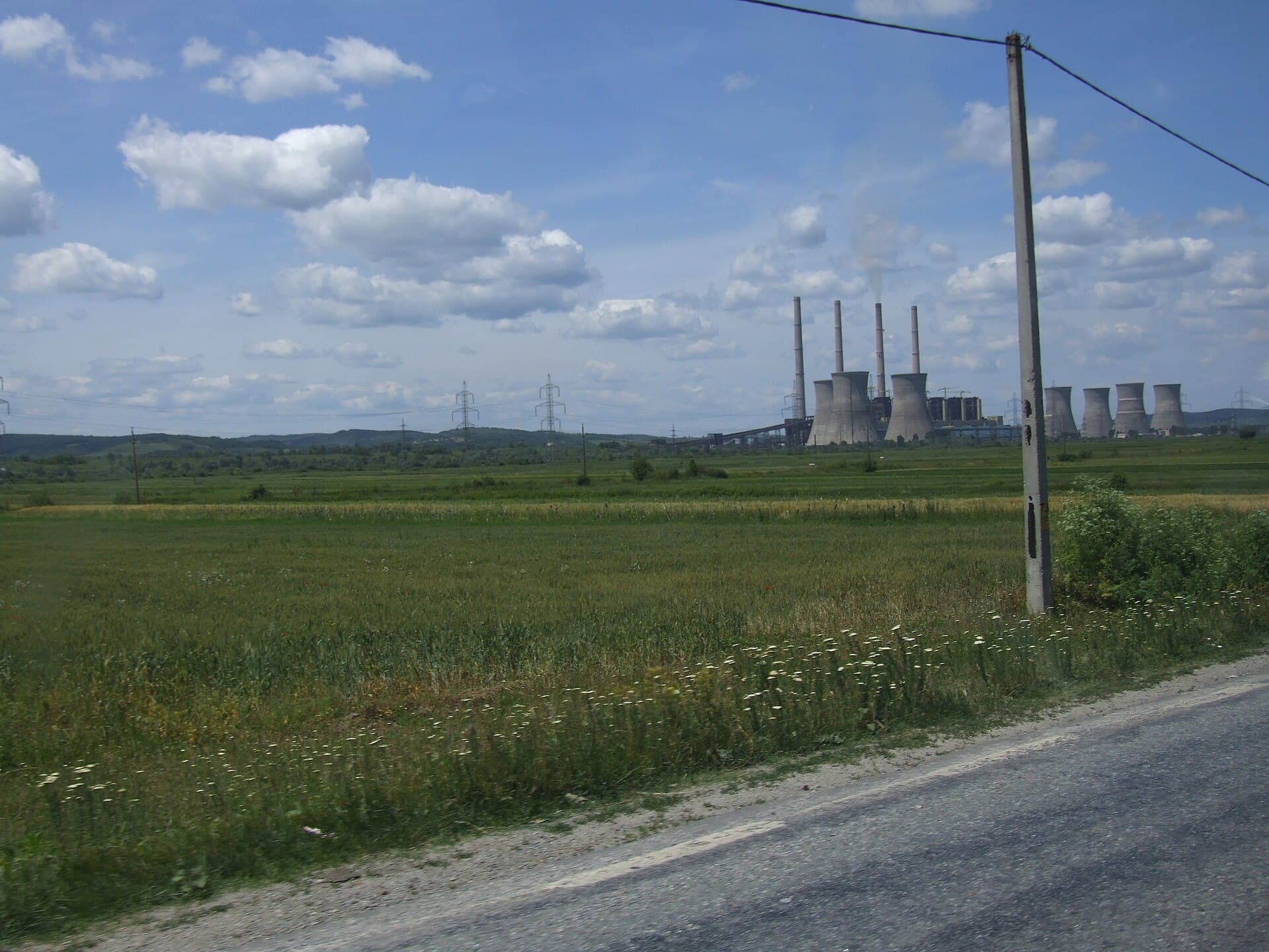O centrală electrică, cu coșuri industriale și turnuri de răcire, văzută de la distanță, într-o zonă rurală. (Foto: CristianChirita / CC BY-SA 2.5, Wikimedia Commons)