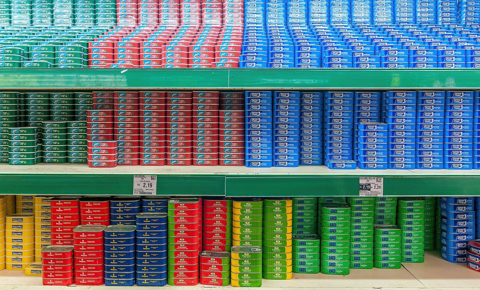 Rafturi de supermarket cu numeroase conserve și etichete de preț. (Foto de arhivă: Wilfredor / CC BY-SA 4.0, Wikimedia Commons)
