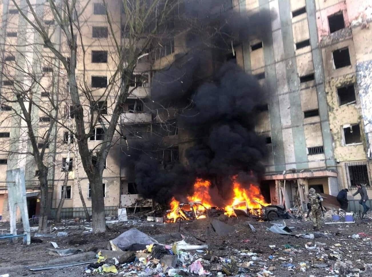 O clădire grav avariată, cu ferestre distruse, incendiu și fum gros, resturi împrăștiate și oameni în apropiere. (Foto: State Emergency Service of Ukraine / BY 4.0, Openverse)
