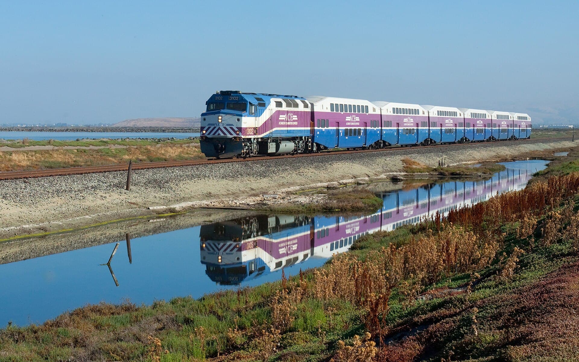 Un tren de pasageri format dintr-o locomotivă și mai multe vagoane, care circulă pe o cale ferată lângă o zonă umedă. (Foto de arhivă: Kabelleger / David Gubler ( http://www.bahnbilder.ch ) / CC BY-SA 3.0, Wikimedia Commons)