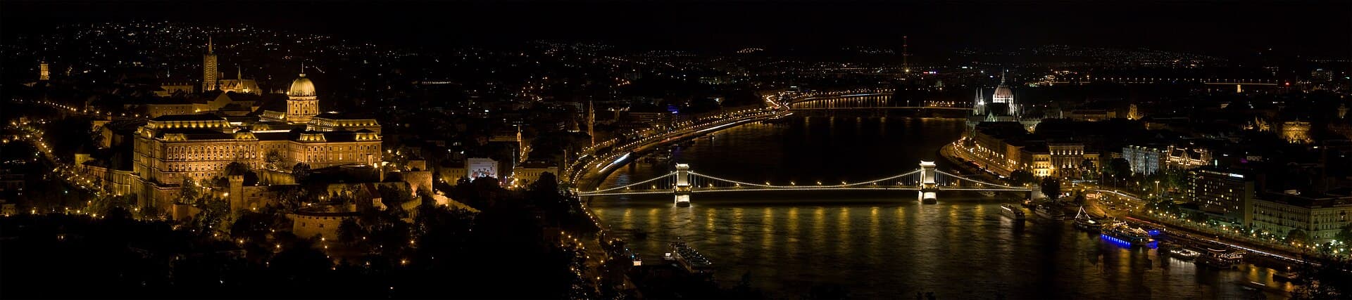 Panoramă nocturnă a Budapestei, cu Dunărea, Podul cu Lanțuri și clădiri iluminate de pe maluri. (Foto: Christian Mehlführer, User:Chmehl / CC BY 3.0, Wikimedia Commons)