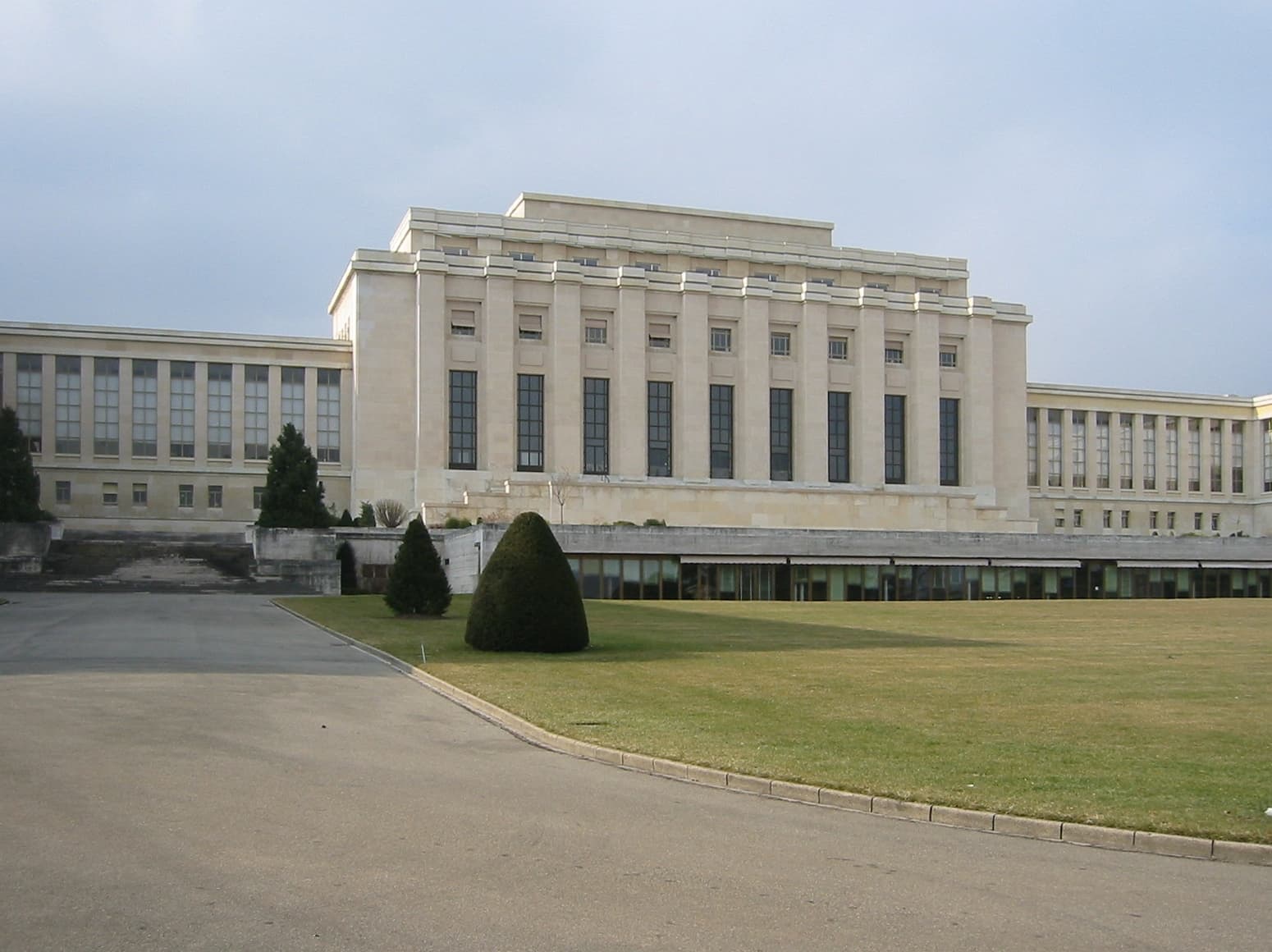 Se vede o clădire instituțională mare, identificabilă ca Palatul Națiunilor al ONU, fotografiată din exterior. (Foto: Yann Forget / CC BY-SA 3.0, Wikimedia Commons)