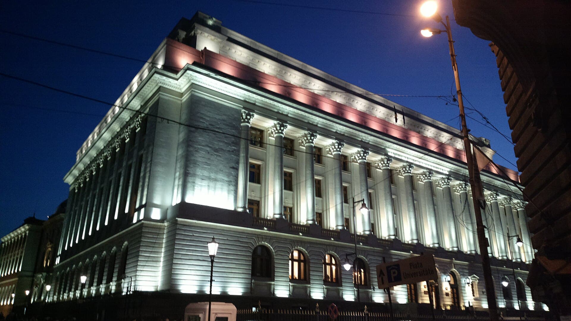 O clădire monumentală iluminată noaptea, cel mai probabil sediul Băncii Naționale a României. (Foto: Korinna / CC BY-SA 3.0 ro, Wikimedia Commons)