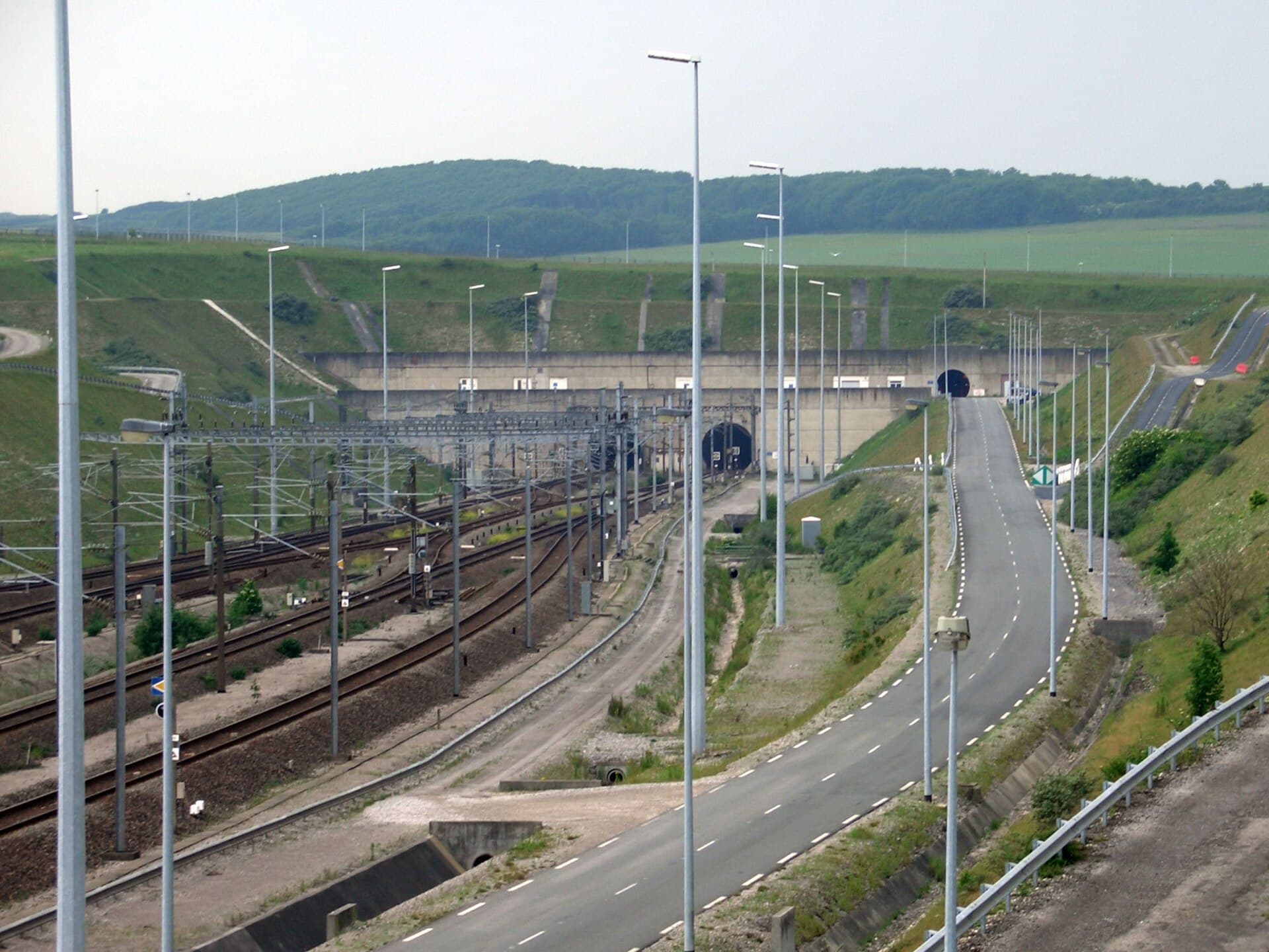 Vedere exterioară a infrastructurii feroviare și a portalurilor Eurotunelului, cu șine și drum de acces; nu sunt vizibile trenul implicat sau urmele accidentului. (Foto: Holger Weinandt / CC BY-SA 3.0 de, Wikimedia Commons)
