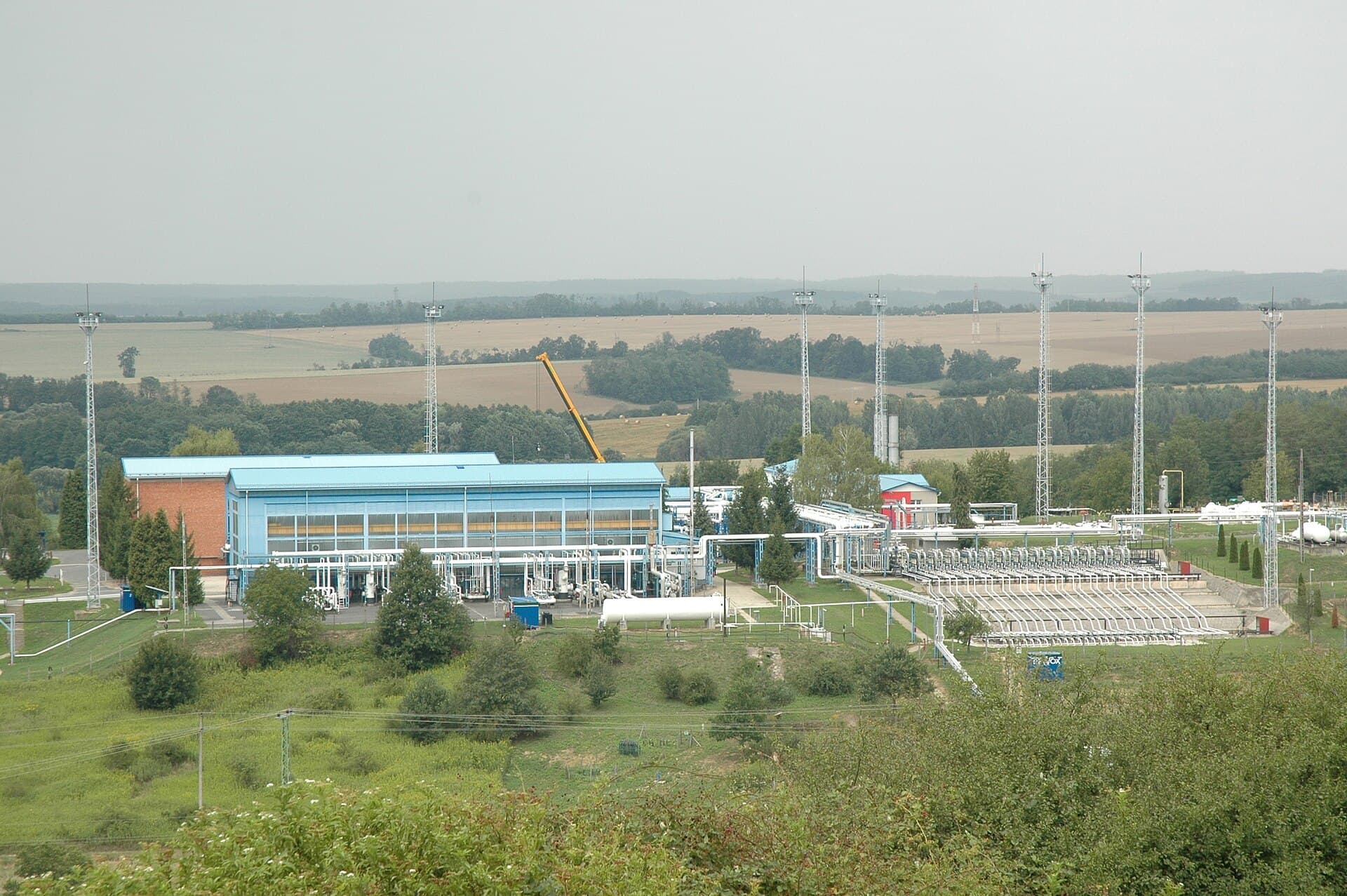 O instalație industrială de gaze, cu clădiri, conducte și echipamente, într-o zonă rurală. (Foto de arhivă: VargaA / CC BY-SA 3.0, Wikimedia Commons)