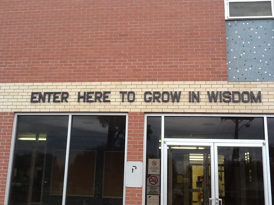 Intrarea unei clădiri școlare, cu inscripția „ENTER HERE TO GROW IN WISDOM” deasupra ușilor. (Foto de arhivă: jdog90 / BY 2.0, Openverse)