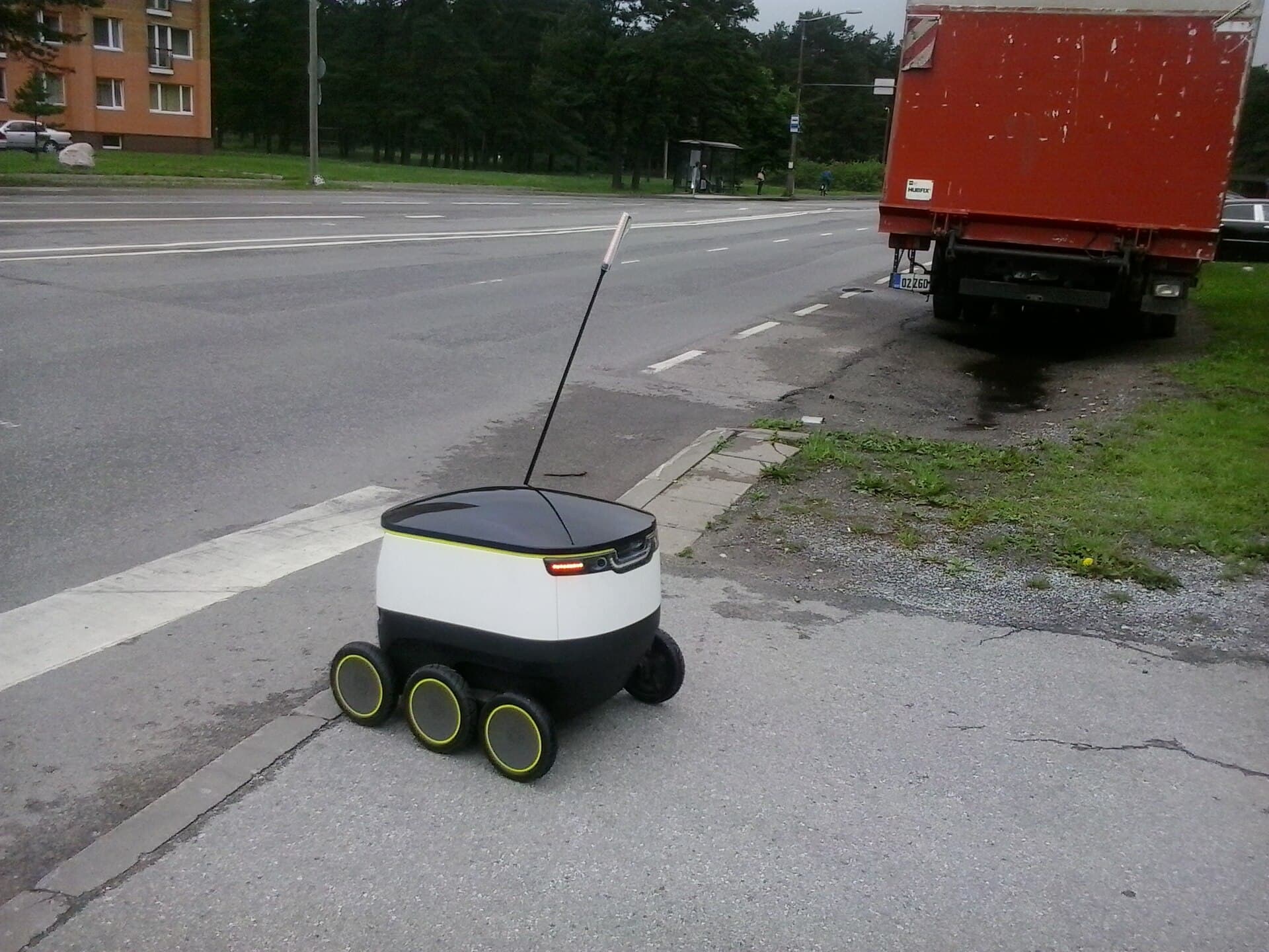 Un robot autonom de livrări pe trotuarul de lângă o stradă urbană, cu un camion parcat în apropiere. (Foto: Photo: Mardus Rover: starship.xyz / CC BY-SA 4.0, Wikimedia Commons)