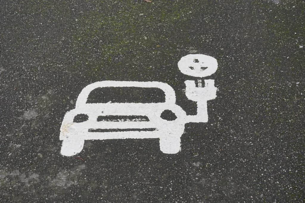 Marcaj rutier alb, stilizat, reprezentând o mașină conectată la o stație de încărcare electrică. (Foto ilustrativă: necunoscut / CC0 1.0, Openverse)