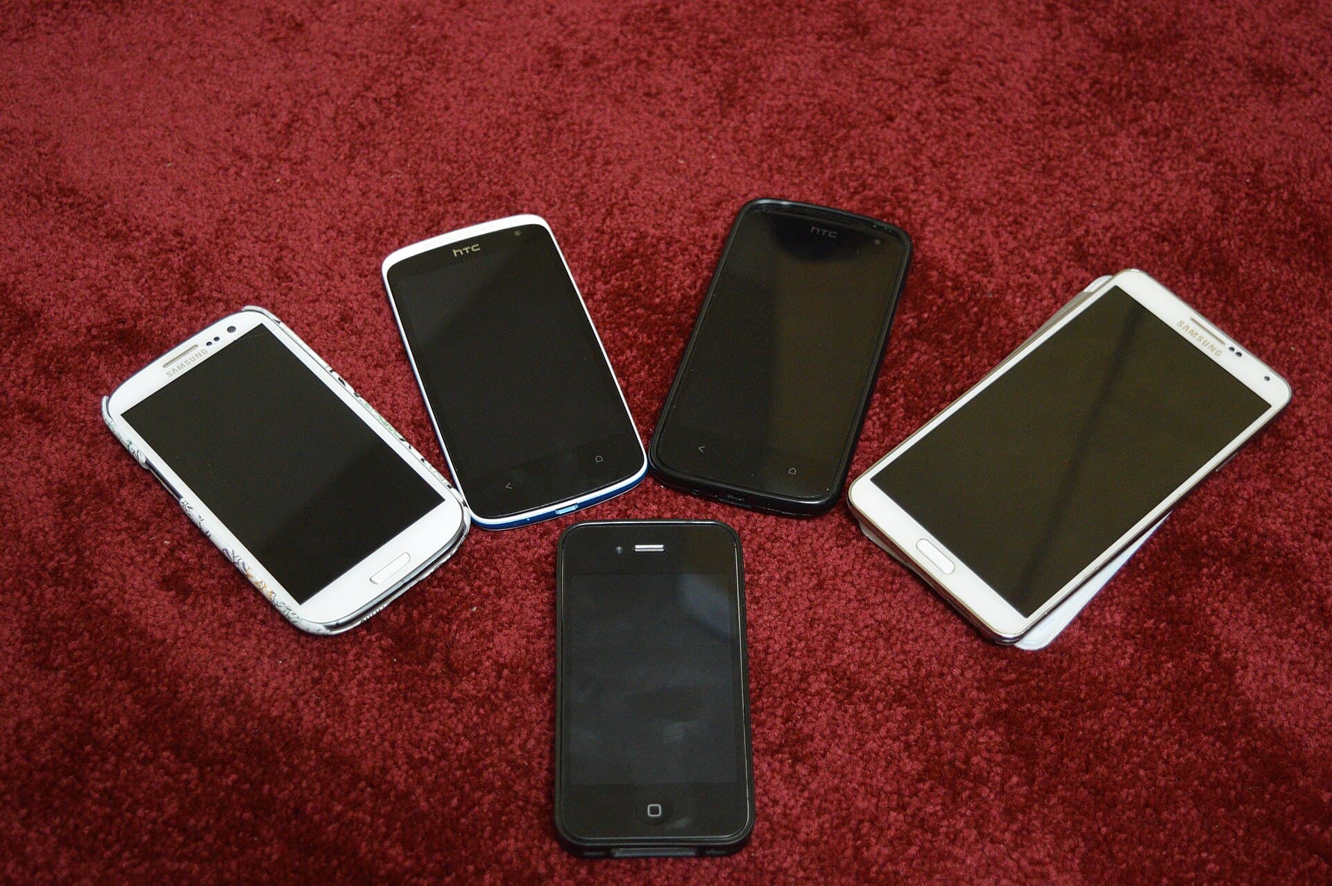 Mai multe telefoane mobile și o tabletă așezate pe o suprafață roșie. (Foto de arhivă: Kskhh / CC BY-SA 4.0, Wikimedia Commons)
