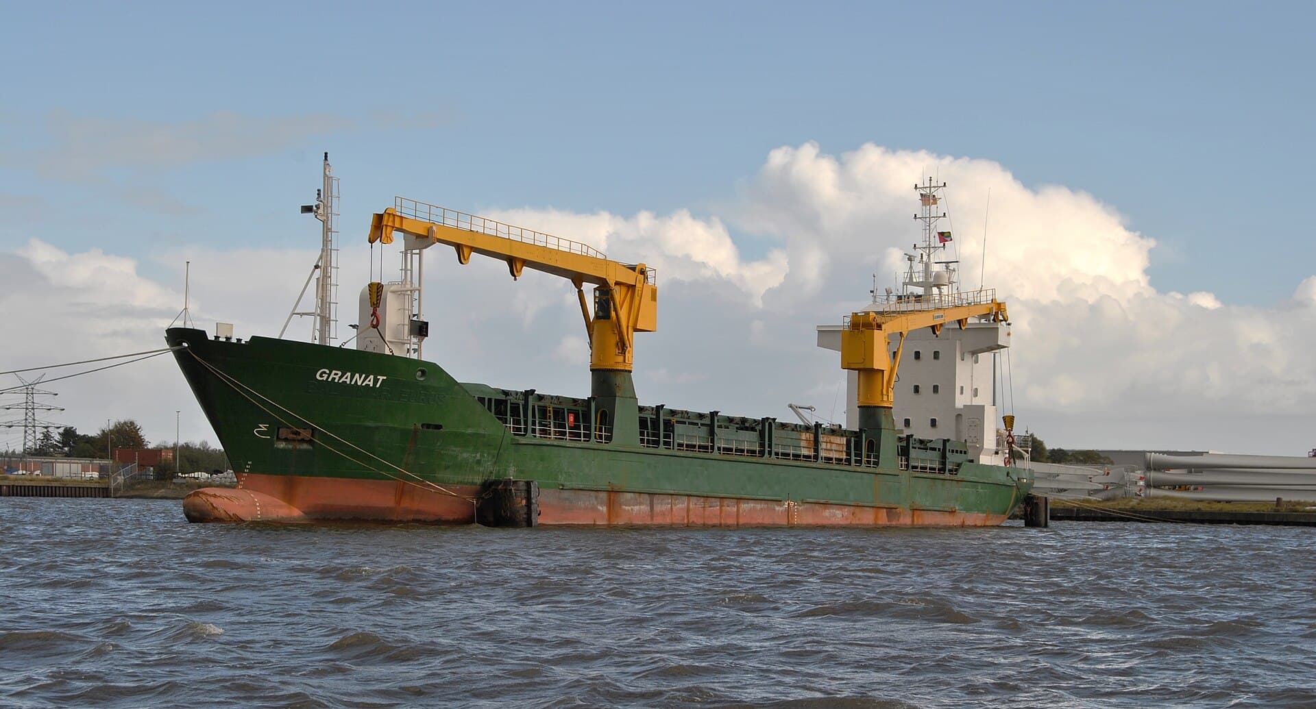 O navă cargo verde, fotografiată pe apă, lângă o zonă portuară. (Foto de arhivă: kaʁstn Disk / Cat / CC BY-SA 3.0 de, Wikimedia Commons)