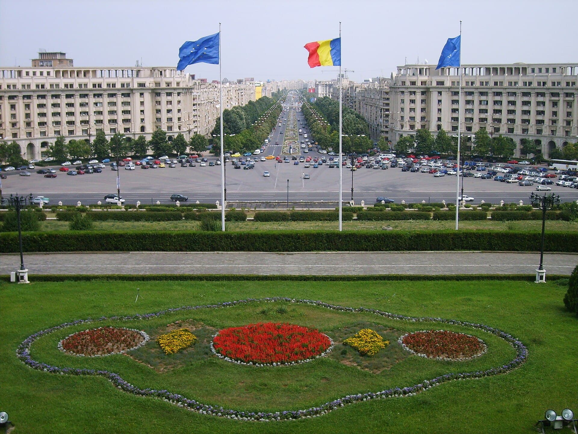 Vedere exterioară a Palatului Parlamentului și a zonei din jur, cu steagurile României și ale Uniunii Europene. (Foto: Alessio Damato / CC BY-SA 3.0, Wikimedia Commons)