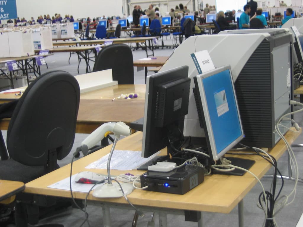O secție de votare, cu mese, cabine și echipamente pentru alegători. (Foto de arhivă: secretlondon123 / BY-SA 2.0, Openverse)