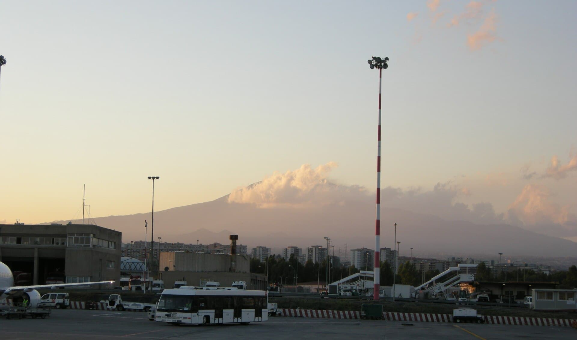 Se vede aeroportul din Catania, cu avioane și autobuze în prim-plan, iar în fundal Muntele Etna fumegând. (Foto: sailko / CC BY 2.5, Wikimedia Commons)