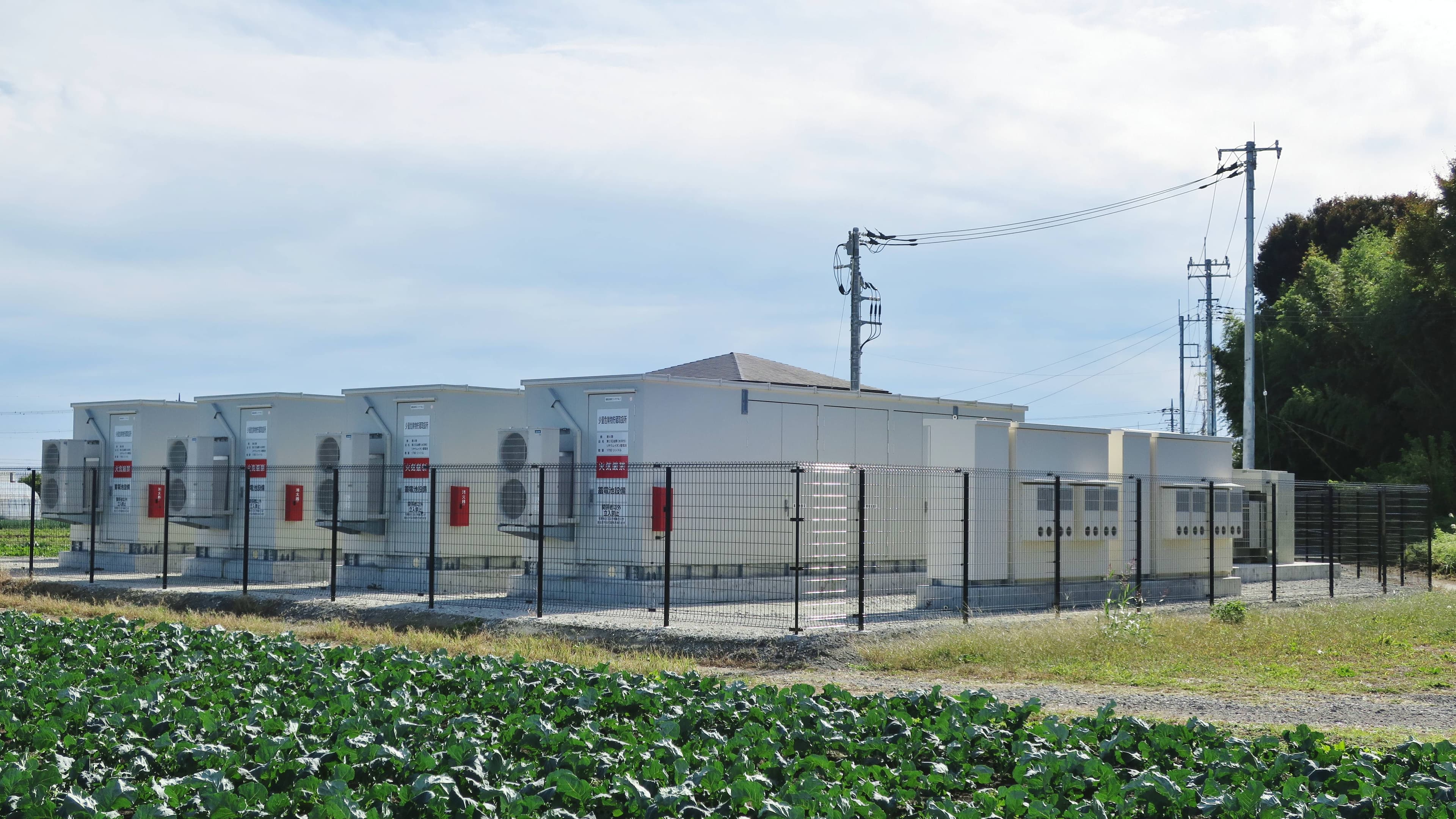 Un șir de containere industriale pentru stocarea energiei, amplasate pe un teren agricol și împrejmuite. (Foto de arhivă: Qurren / BY-SA 4.0, Openverse)