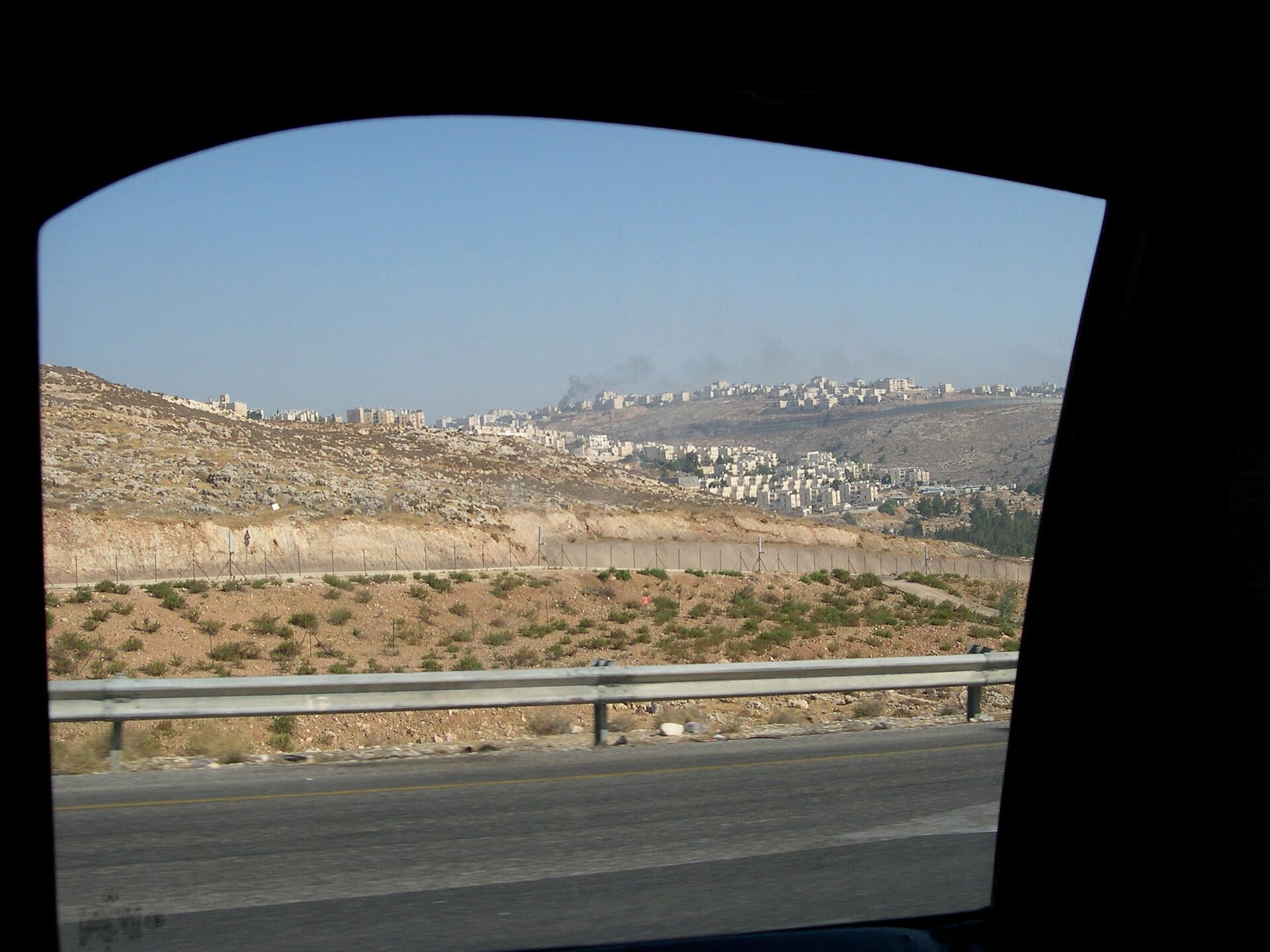 Peisaj de dealuri aride și o zonă urbanizată, fotografiată de pe șosea, probabil în Cisiordania. (Foto: upyernoz from Haverford, USA / CC BY 2.0, Wikimedia Commons)