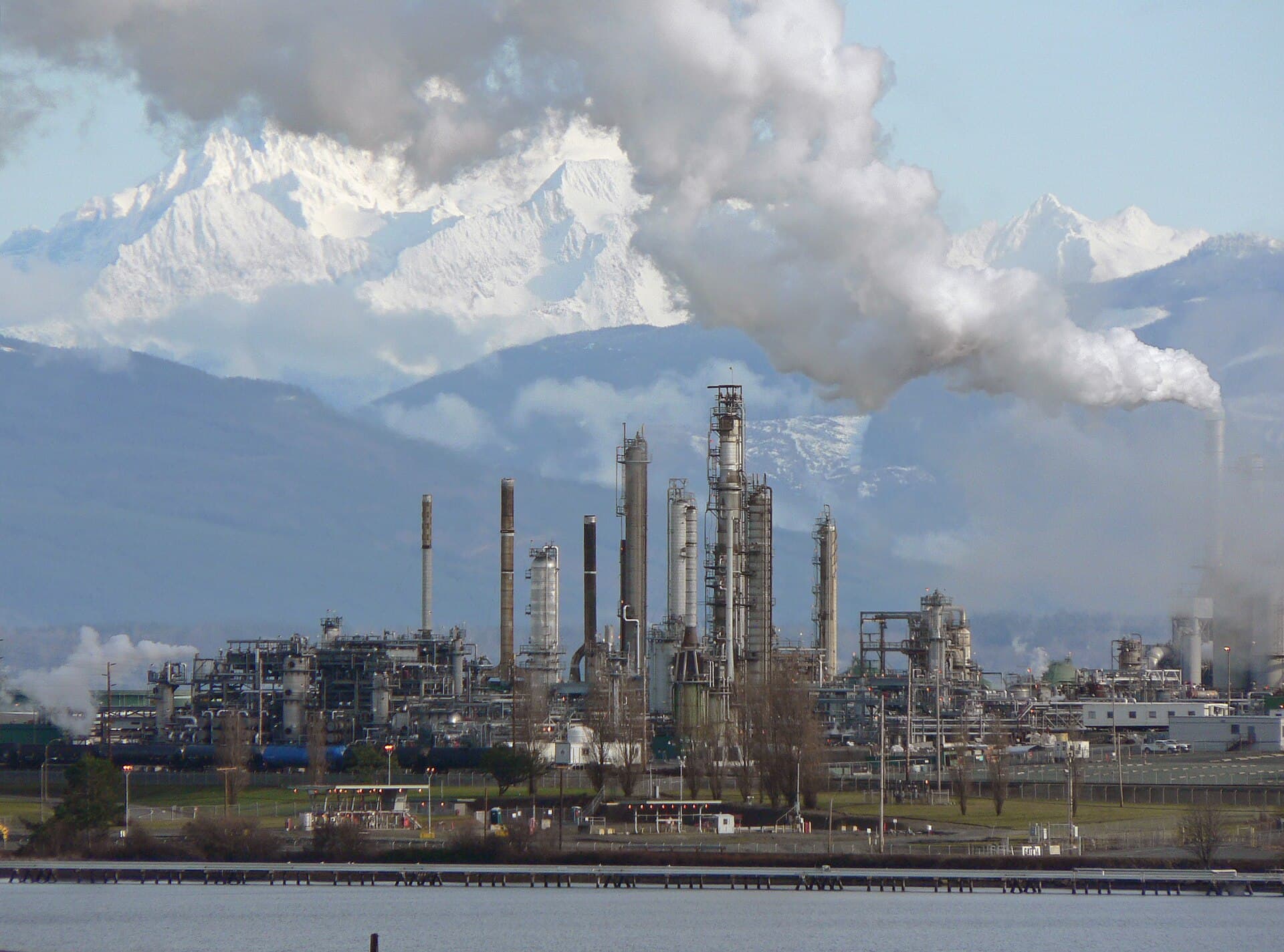 O rafinărie industrială cu coșuri și instalații, din care se ridică fum, pe fundalul unor munți. (Foto de arhivă: Walter Siegmund (talk) / CC BY 2.5, Wikimedia Commons)