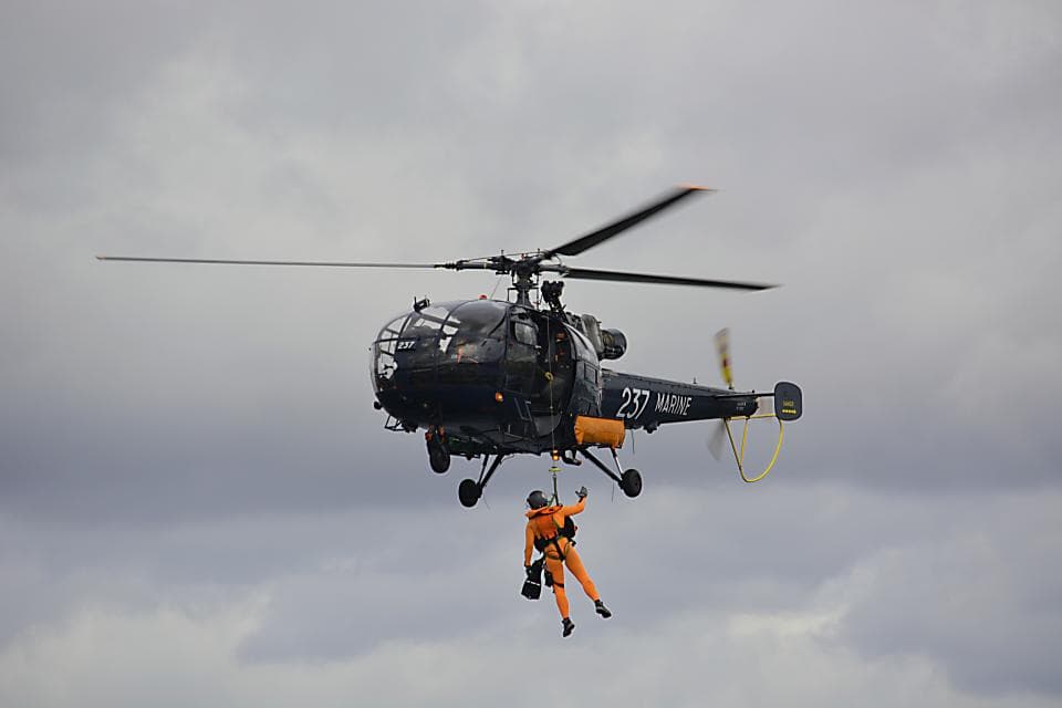Un elicopter militar în zbor, cu o persoană suspendată dedesubt, probabil într-un exercițiu de salvare. (Foto ilustrativă: Richard Revel / CC0 1.0, Openverse)
