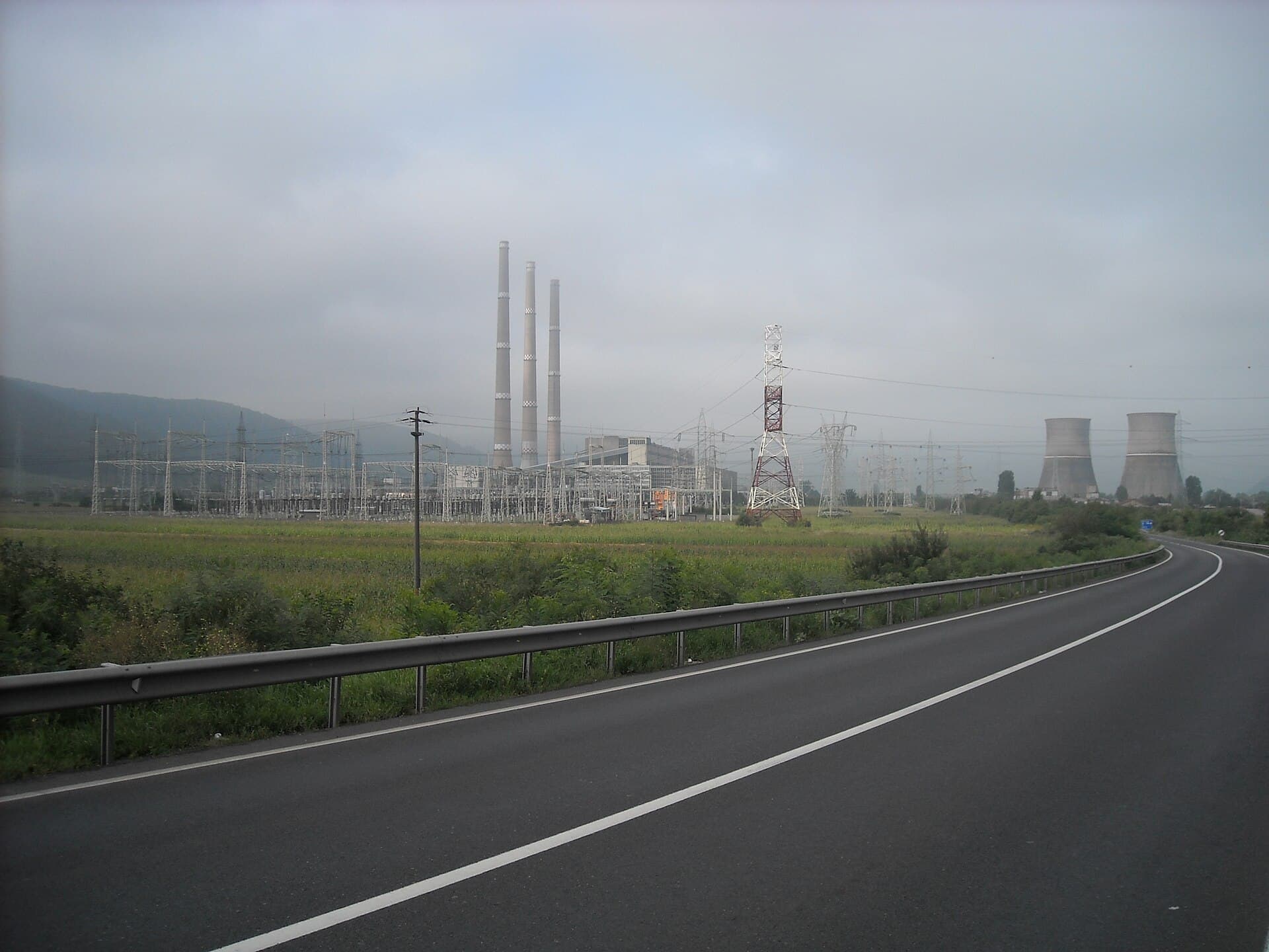 O centrală energetică industrială, cu coșuri de fum, instalații electrice și turnuri de răcire, văzută de pe un drum. (Foto: Oguszt / CC BY-SA 3.0, Wikimedia Commons)