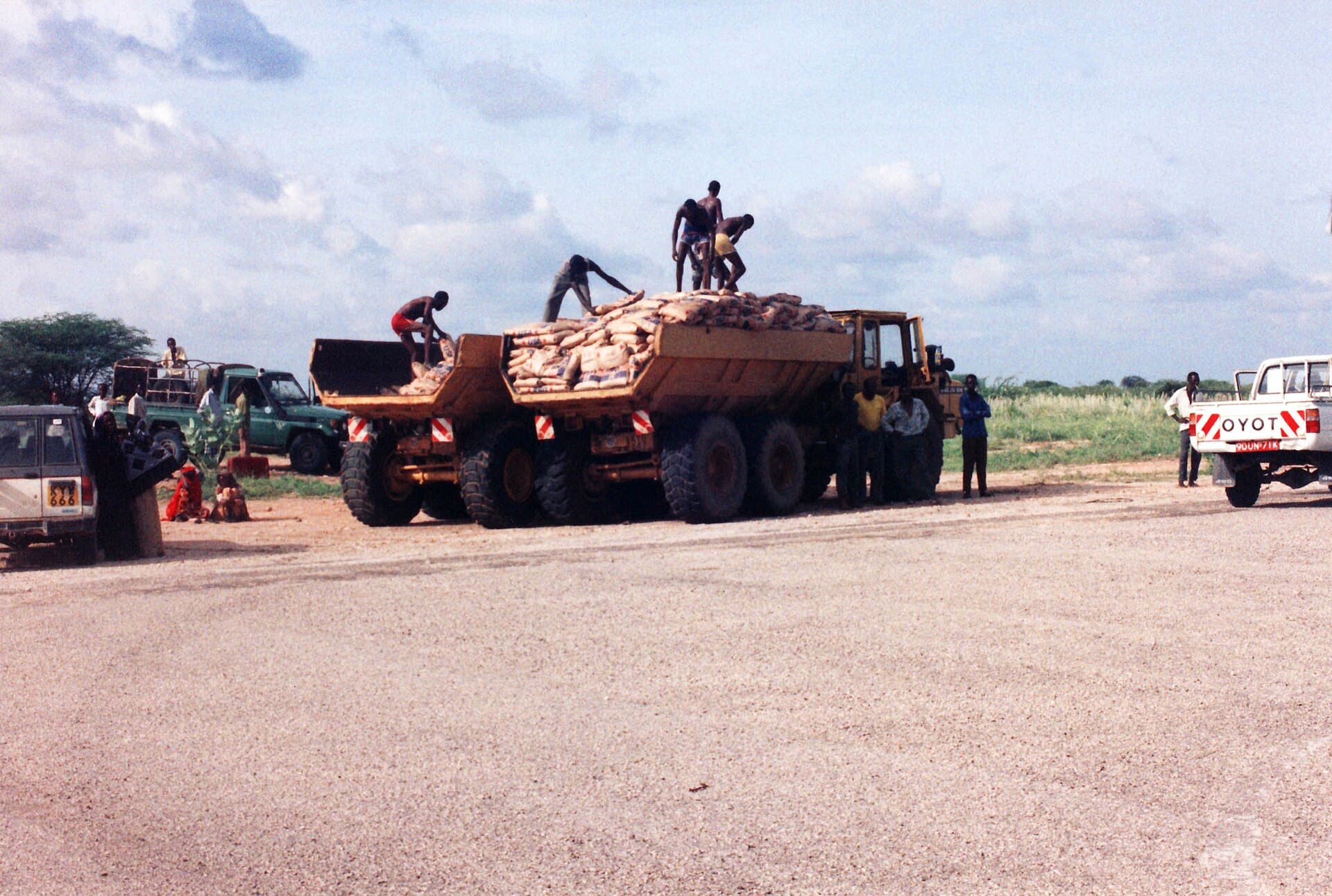 Un vehicul blindat încărcat cu saci, oameni care manipulează ajutoare și alte vehicule într-o zonă rurală din Africa. (Foto de arhivă: Monica's Dad / CC BY 2.0, Wikimedia Commons)