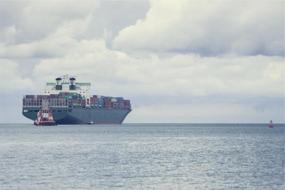 O navă comercială mare, încărcată cu containere, este escortată sau manevrată de un remorcher pe mare. (Foto ilustrativă: Martin%20D%F6rsch / CC0 1.0, Openverse)