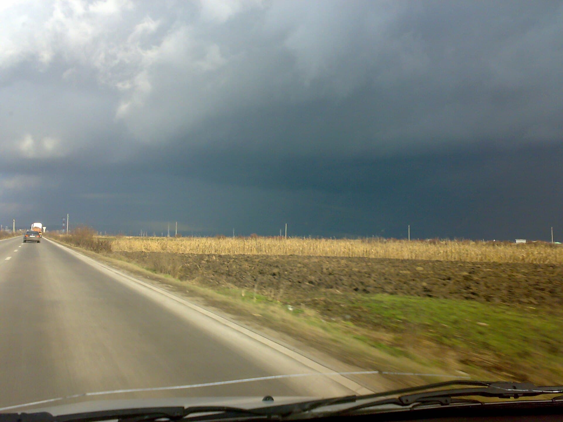 Un drum de țară printre câmpuri agricole, sub un cer întunecat și înnorat. (Foto: SEBASTIAN DUMITRESCU / CC BY-SA 3.0, Wikimedia Commons)